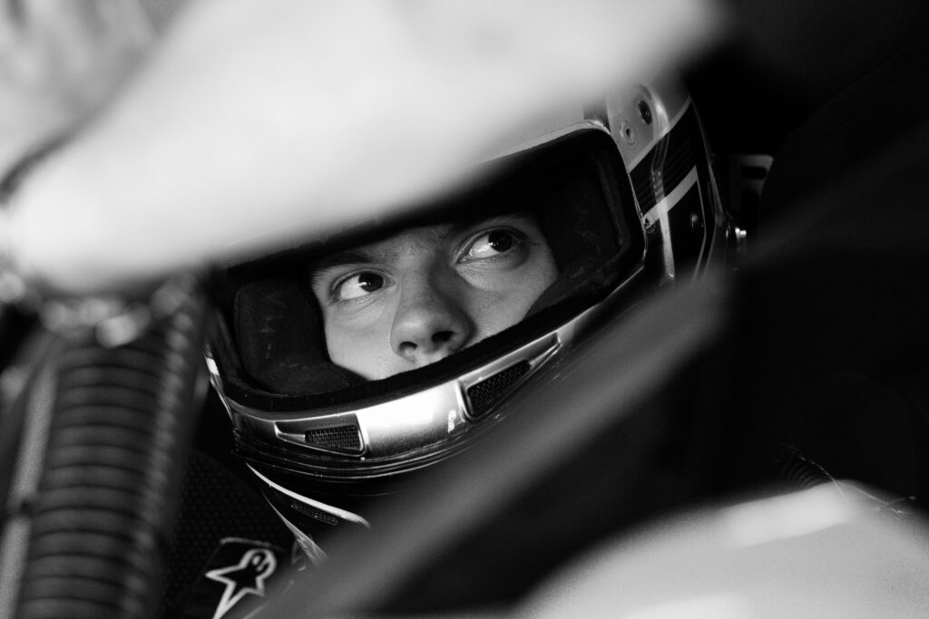 Black and white photo of a race car driver intensely focused, wearing a helmet.